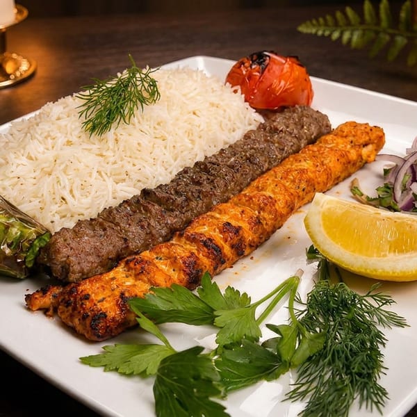 White plate with two kebabs, fluffy rice, grilled pepper, tomato, lemon, and onion salad.