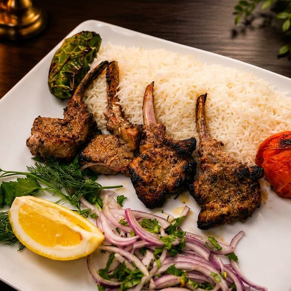 Plate of grilled lamb chops, white rice, roasted tomato, pepper, lemon, and red onion garnish.